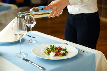 Waiter serve restaurant table with salad and wineの写真素材