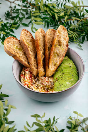 Hummus bowl with sliced avocado and toastsの写真素材
