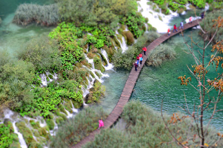 Scenic top-down view of lush greenery, multiple waterfalls, and a winding wooden trail over turquoise waters in Plitvice Lakes National Park, a UNESCO World Heritage Site.の写真素材