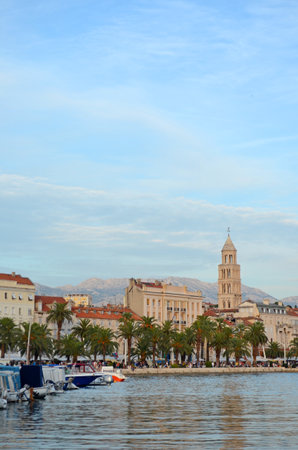 Scenic view of Split's historic waterfront featuring Diocletian's Palace, the bell tower of Saint Domnius Cathedral, palm trees, boats, and the calm Adriatic Sea.の写真素材