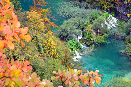 Scenic top-down view of lush greenery, multiple waterfalls, and a winding wooden trail over turquoise waters in Plitvice Lakes National Park, a UNESCO World Heritage Site.の写真素材