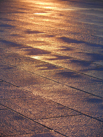 Close-up of wet stone pavement glistening under sunlight, with golden highlights and irregular reflectionsの写真素材