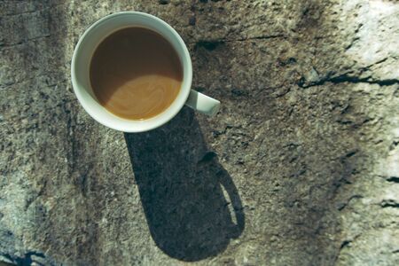 Top view of coffee cup placed on the stone bench in the morning with soft sunlight.