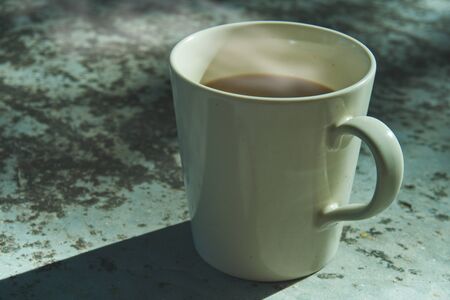 In the morning, a coffee cup placed on the marble table with soft sunlight.の写真素材