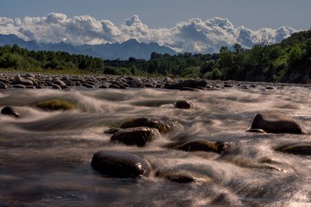 Amazing long exposure landscape photograph near Cuneo in Italy with everything that a nice view needs: a river, rocks, forest, mountains and dramatic clouds.の写真素材