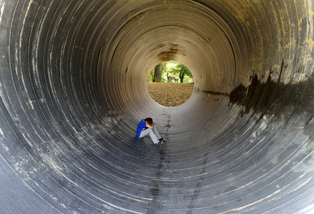 depressed child sitting in the large drainage pipeの写真素材