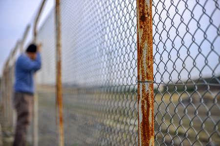 wire fence in front sad poor man standingの写真素材