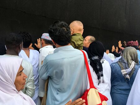 MECCA, SAUDI ARABIA - JUNE 28: Unidentified Muslim pilgrims in white ihram touch black cloth of Kaaba with Allah and Muhammad (peace be upon him) inscriptions on June 28, 2019 in Mecca Saudi Arabia.のeditorial素材