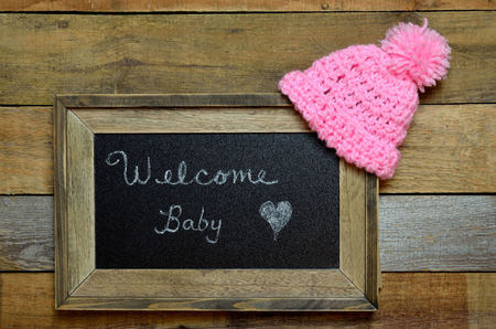 Welcome sign for baby girl.  Pink knit hat draped over framed sign.の写真素材