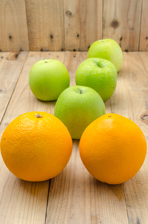 Green apples and orange on wooden panelの写真素材