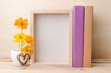 Photo frame with books and flowers on the wooden table