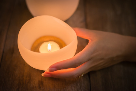 Candle in young woman hands on wooden backgroundの写真素材