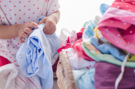 Baby with heap of colorful clothes in the roomの写真素材