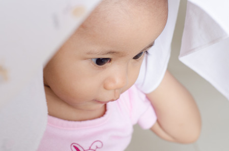 Happy little baby girl hidden her face in white cloth diaperの写真素材