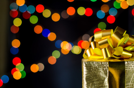 Gold christmas gift box with ribbon and bow on bokeh lights background