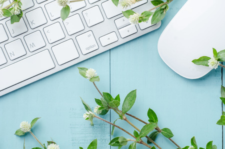 Top view of wooden working table with computer keyboard, mouse and wild flowers . View from above with copy space.の写真素材