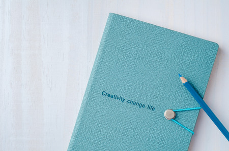 Blue notebook with color pencil on white wooden background