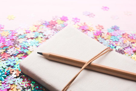 Notebook with pencil on heap of colorful plastic flower for decoration.の写真素材