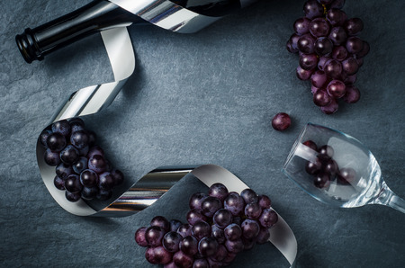 Wineglass , bottle with ripe grapes and ribbon on black stone background.の写真素材