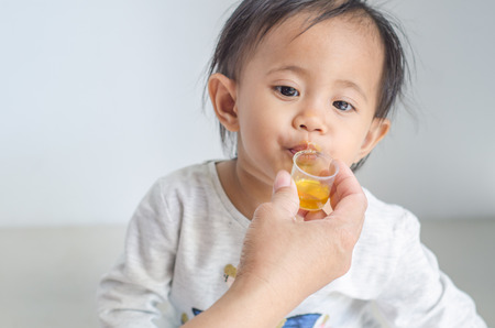 Asian little girl takes medicine syrup with her motherの写真素材