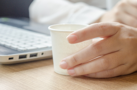 Woman working with laptop and hand holding paper glass of waterの写真素材