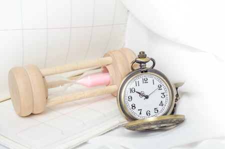 Vintage pocket watch with hourglass on white fabric background