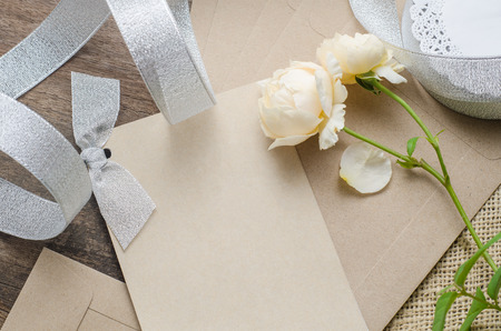 Blank invitation card with brown envelope and rose flowers on wooden backgroundの写真素材