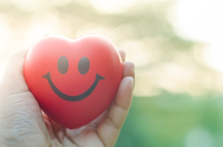 Close up hand holding smile red heart with light backgroundの写真素材