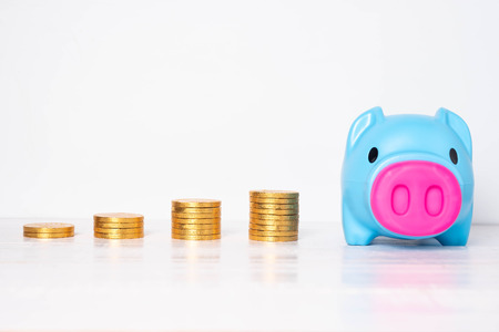 Blue piggy bank with piles of golden coins  on white background. Saving money concept.の写真素材