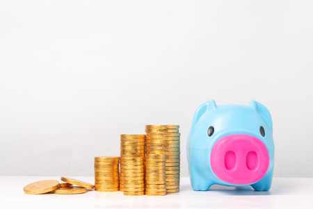 Blue piggy bank with piles of golden coins  on white background. Saving money concept.の写真素材