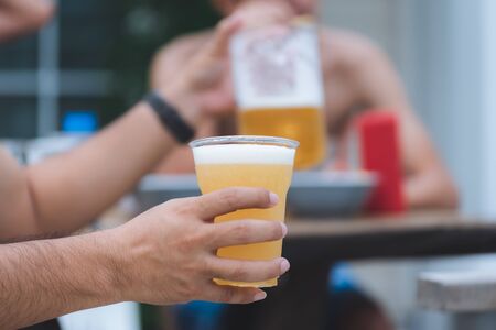 Close up hands of unidentified man pouring beer from pitcher to plastic glass at home yardの写真素材