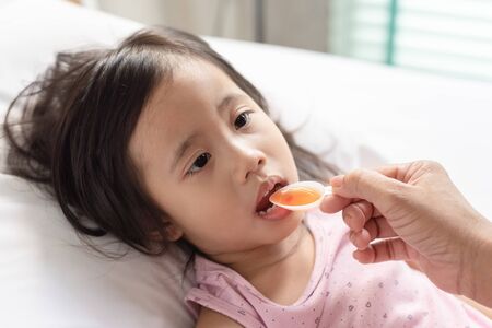 Unhappy asain girl when taking medicine syrup from her motherの写真素材