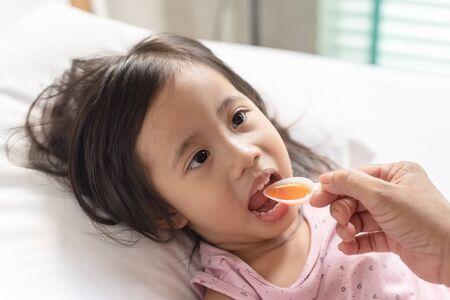 Little asain girl taking medicine syrup from her motherの写真素材