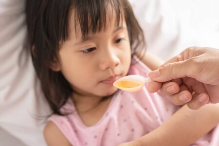 Unhappy asain girl when taking medicine syrup from her motherの写真素材
