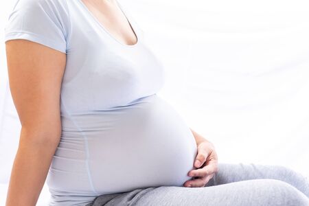 Close up pregnant women sitting and touching her belly with hands on white background.