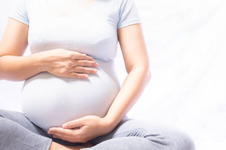 Close up pregnant women sitting and touching her belly with hands on white background.の写真素材
