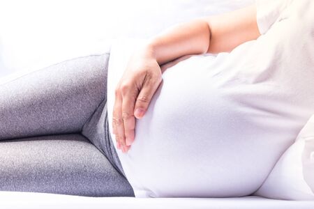 Close up pregnant women lying and touching her belly with hands on her bed.