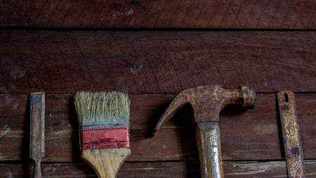 old wooden board with old rusty carpentry tools: hammer, paint brush, chisel, hacksaw, mortar