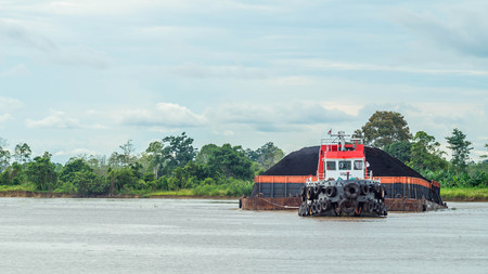 Tugboats pull heavy load barge of black coal in Mahakam river, Borneo, Indonesiaの写真素材
