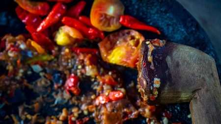traditional Indonesian chili sauce, fried chili, tomato, onion, and shrimp paste crushed on stone mortar with wooden pestleの写真素材