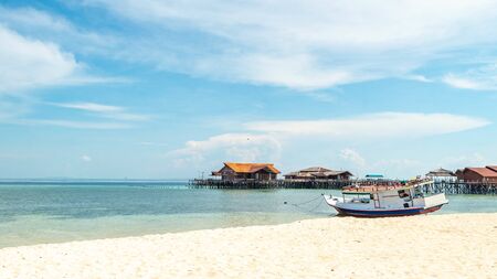 Beautiful view of crystal clear water, white sand, blue sky, traditional cottage, and wooden boat at Derawan Island, Indonesiaの写真素材
