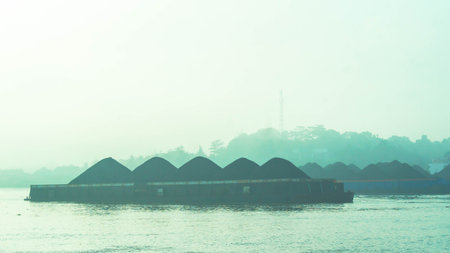 Misty morning in Mahakam river, tugboat dragging barge full of coal, Samarinda, Indonesia.の写真素材