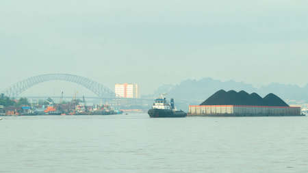 Tugboat drag barge full of coal crossing Mahakam River, Samarinda, in the morning. Transportation and industrial backgroundの写真素材
