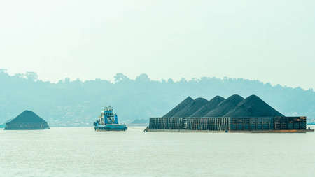 Tugboat drag barge full of coal crossing Mahakam River, Samarinda, in the morning. Transportation and industrial backgroundの写真素材