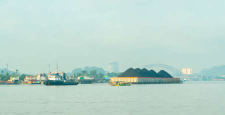 Tugboat drag barge full of coal crossing Mahakam River, Samarinda, in the morning. Transportation and industrial backgroundの写真素材