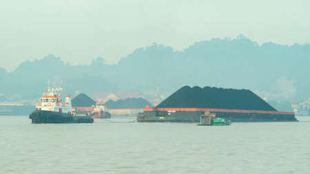 Tugboat drag barge full of coal crossing Mahakam River, Samarinda, in the morning. Transportation and industrial backgroundの写真素材