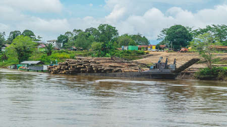 Timber loaded into big barge then drag by a tugboat cruising Mahakam River, Borneo, Indonesiaの写真素材