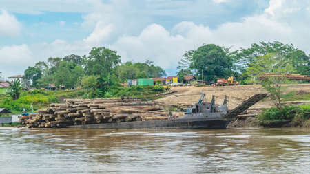 Timber loaded into big barge then drag by a tugboat cruising Mahakam River, Borneo, Indonesiaの写真素材