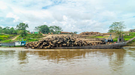 Timber loaded into big barge then drag by a tugboat cruising Mahakam River, Borneo, Indonesiaの写真素材