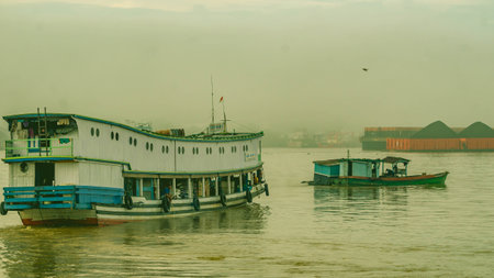 Long wooden boat loaded by passengers and goods cruising Mahakam River, East Borneo. This wooden...